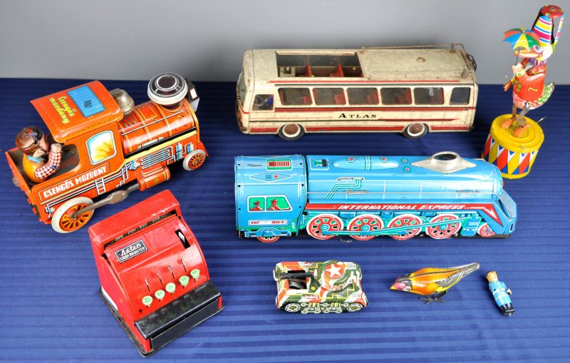 Een lot oud blikken speelgoed, bestaande uit een eend met paraplu, een bus, twee treinen, een vogeltje, een tank, een speelgoedkassa en een soldaatje.