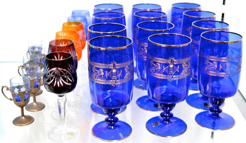 Lot glas en kristal, bestaande uit een serie van 12 grote glazen van blauw Boheems glas met een gegraveerd en verguld motief  van strijdwagens, zes sherryglaasjes van geslepen kristal met diverse kleuren en vier borrelglaasjes van blauw glas met koperen houdertjes met oor.