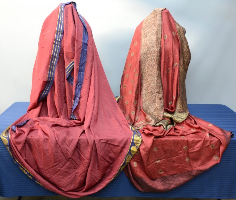 Twee wijnrode sari’s van zijde, beide afgeboord met gouddraad. Indisch werk. Enige slijtage.