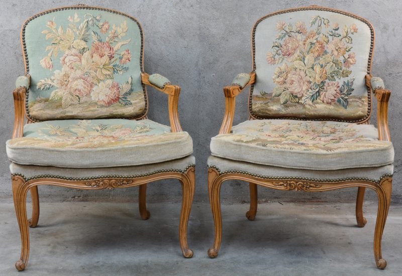 Een paar fauteuils à la reine van gesculpteerd eikenhout in Lodewijk XV-stijl, bekleed met naaldwerk.
