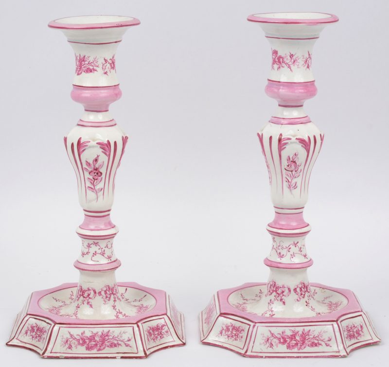 Een paar kandelaars van roze en wit aardewerk, versierd met een bloemendecor. Onderaan gemerkt. Eén met haarscheur bovenaan.