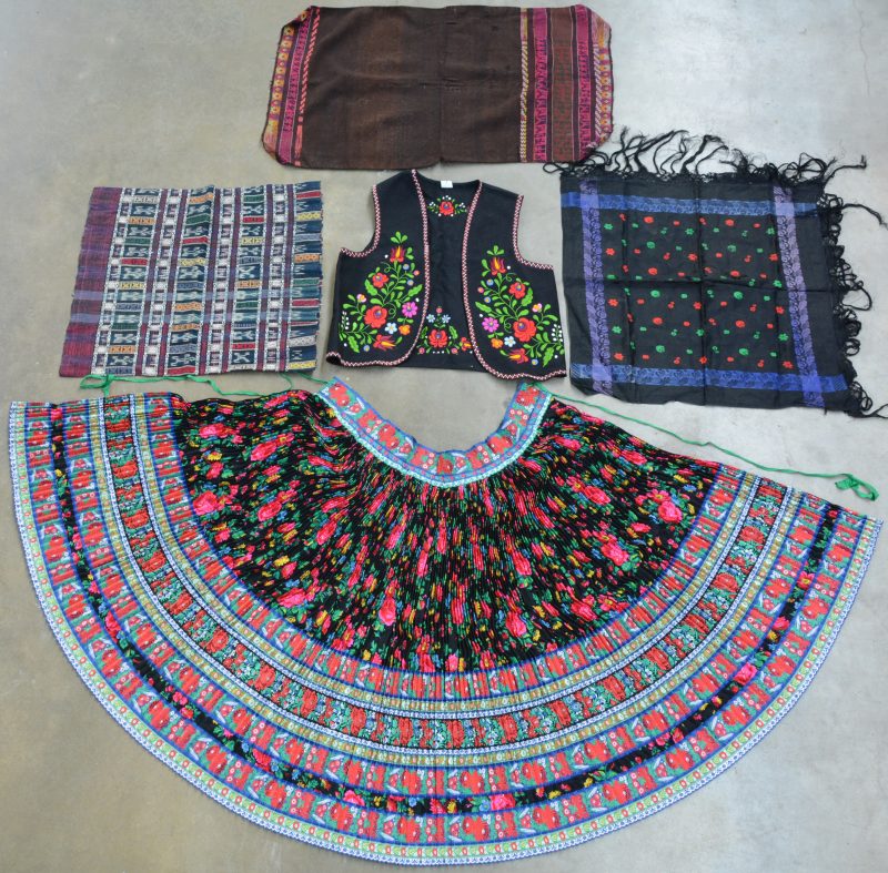Een lot textiel bestaande uit een gilet, een sjaal en een grote plooirok met bloemmotief uit Hongarije. Evenals een Centraal-Europese kussensloop en een tapijtje van geweven wol.