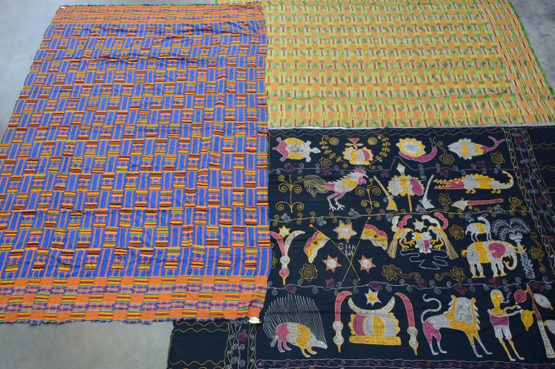 Twee Keniaanse kleden in veelkleurig patchwerk en één met geborduurde dieren en personages.