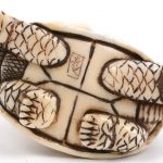 “Man op schildpad”. Een netsuke van gesculpteerd ivoor op houten sokkeltje. Onderaan gesigneerd. We voegen er een tweede netsuke van gesculpteerd hout in de vorm van een draak aan toe.