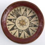 Een oud kompas in een gedraaide houten houder met deksel.