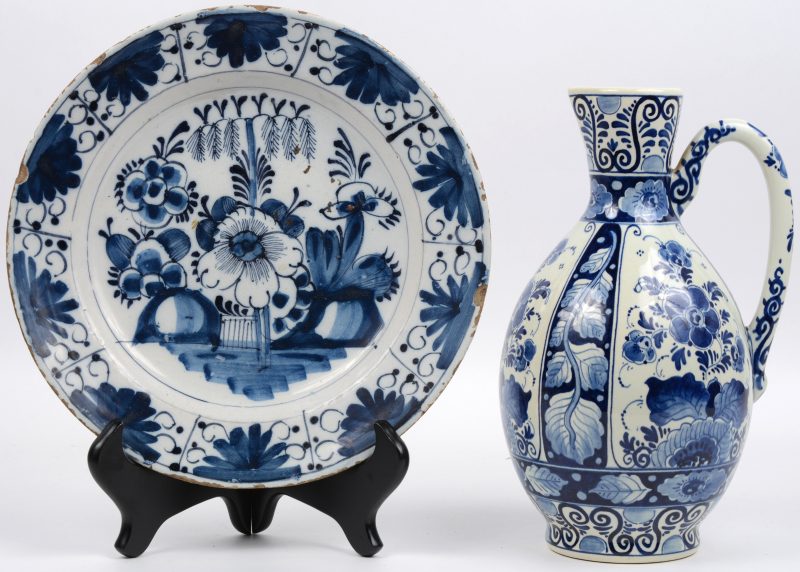 Een schotel van blauw en wit Delfts aardewerk, versierd met een bloemendecor. XIXe eeuw. We voegen er een recente Delftse schenkkan aan toe.