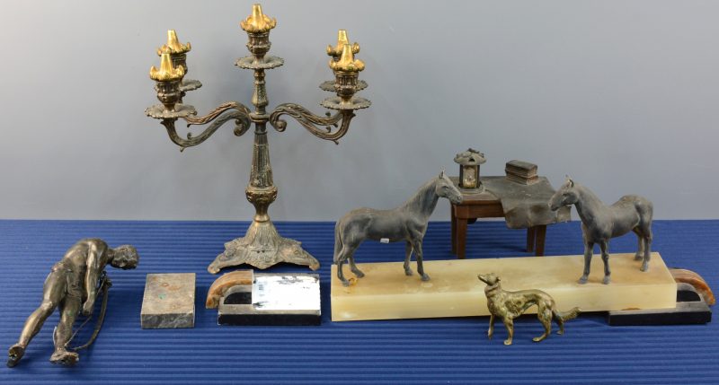 Een lot varia, bestaande uit een sokkel van albast en marmer met twee zamakken paardjes, een kandelaar met vijf lichtpunten, een tafeltje met een lantaarn, een bronzen hondje en een boogspanner van zamak. Beschadigingen en manco’s.