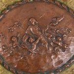 Een bronzen milieu-de-table met een opengewerkt decor van bladeren met hoofdjes op de handvatten. In het midden een gedreven koperen reliëf met een voorstelling van Venus met engeltjes. Omstreeks 1900.