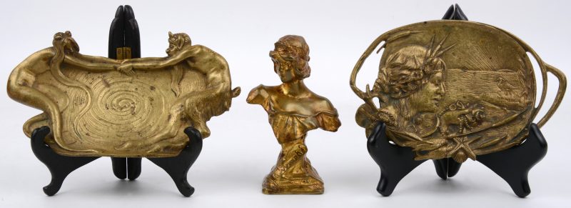Een jongedamesbuste getiteld “Nymphe” en twee vide-poches, waarvan één met een voorstelling van een jonge vrouw en een reiger en de andere met een dansen naakt en een sater.  Beide van goudgepatineerd brons. Tijdperk art nouveau.