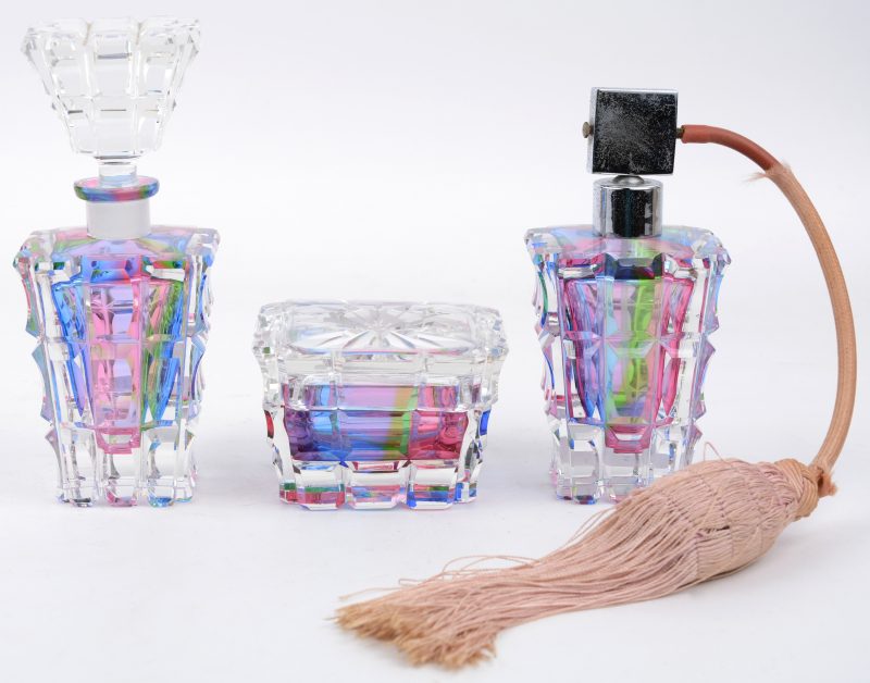Een driedelig toiletstelletje van meerkleurig kristal, bestaande uit een dekseldoosje, een parfumverstuiver en een flesje.