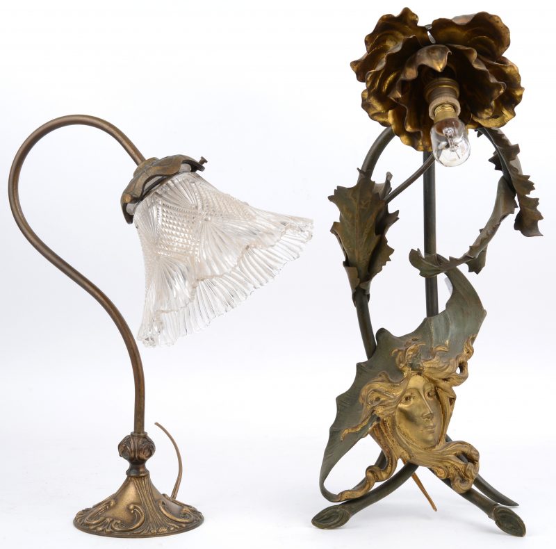 Een paar koperen lampjes, waarbij één met een glazen kapje en het andere in art nouveaustijl, versierd met een vrouwenhoofd.