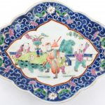 Een schaaltje op voet van meerkleurig Chinees porselein met een decor van personages en met bloemen op blauwe fond op de rand. Onderaan gemerkt.
