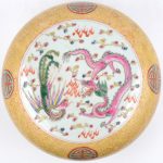 Een dekselschaal van meerkleurig Chinees porselein met een decor van een draak en een vogel in een ronde cartouche in een gele achtergrond.