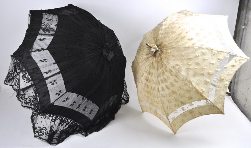 Twee oude parasols van wit en zwart kant een paar zwarte veren en een zijden stola met borduurwerk.