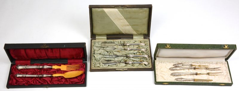 Drie etuis met zilveren bestekken, waarvan een slabestek met been, een vierdelig visbestek en één met drie vorken en een mes.