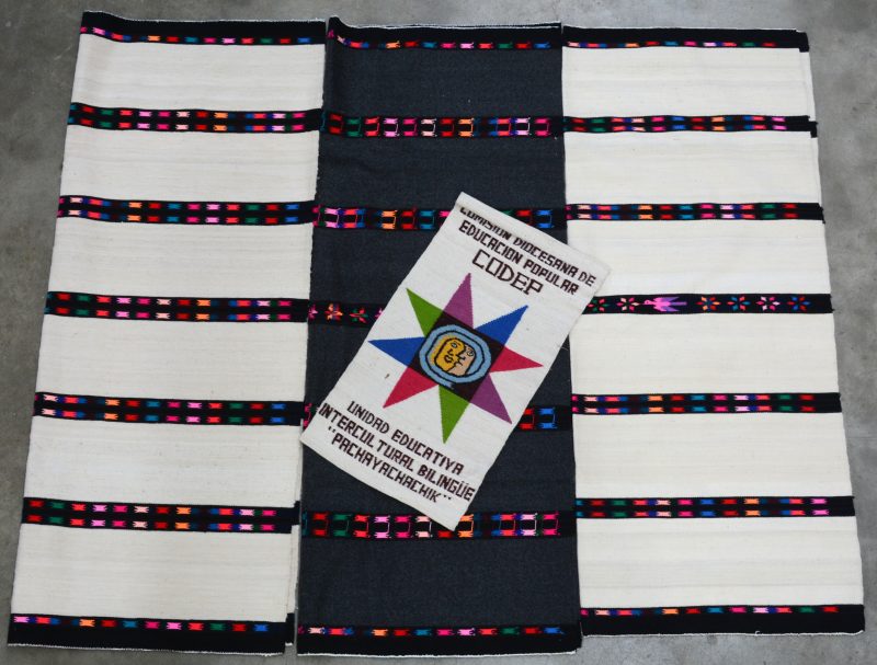 Drie kleedjes uit de Andes met veelkleurige stroken. En een kleine lap met “Codep, Unidad Educativa Intercultural Bilingüe “Pachayachachik”.