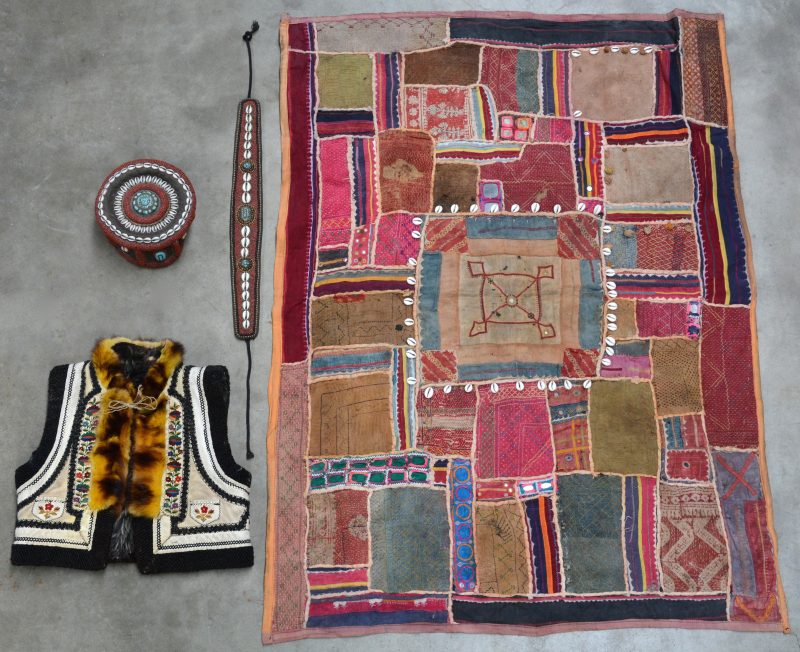 Een Afrikaans patchwerk, een Afrikaanse gordel en muts met kralen en schelpen en een vestje van gekeerd schaap met borduurwerk.