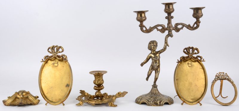 Een lot verguld koper en brons, bestaande uit drie ovale fotokadertjes, een kandelaar gedragen door een putto, een kandelaar in Lodewijk XV stijl en een versiering in de vorm van een acanthusblad.