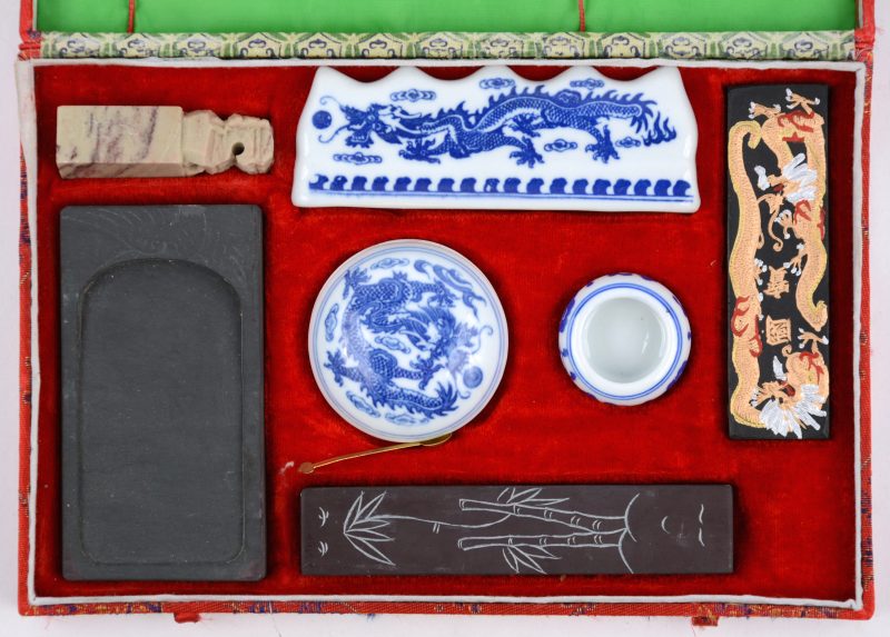 Een Chinese kaligrafische set, bestaande uit een waterbakje en een stempel van leisteen, een penseellegger, een verfbakje en een waterkommetje van porselein met een draak in het decor en een stempel van speksteen. In etui.