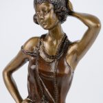 Een bruingepatineerd bronzen beeldje in de vorm van een jonge vrouw in art deco klederdracht.