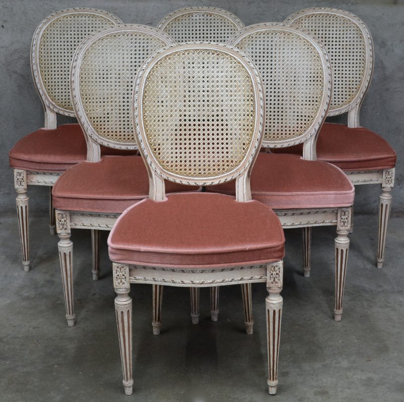 Een reeks van zes stoelen van gesculpteed en witgepatineerd hout in Lodewijk XVI-stijl met gecanneerde rug en zit.