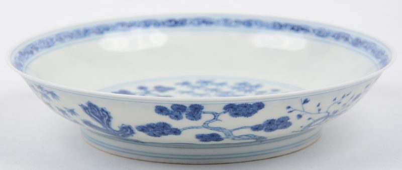 Een diep bord van blauwe en wit Chinees porselein met een decor van planten. Onderaan gemerkt.