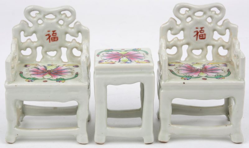 Een paar miniatuur armstoeltjes met bijhorend tafeltje van monochroom wit porselein, versierd met een polychrome bloem.