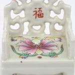 Een paar miniatuur armstoeltjes met bijhorend tafeltje van monochroom wit porselein, versierd met een polychrome bloem.