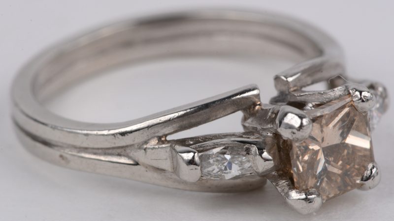 Een 18 karaats wit gouden ring bezet met een in princes geslepen cognac kleurige diamant van ± 0,60 ct. en twee in markies geslepen diamanten met een gezamenlijk gewicht van ± 0,20 ct.