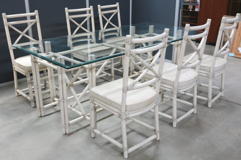 Een tafel van witgepatineerd bamboe met glazen blad en met zes bijpassende stoelen.