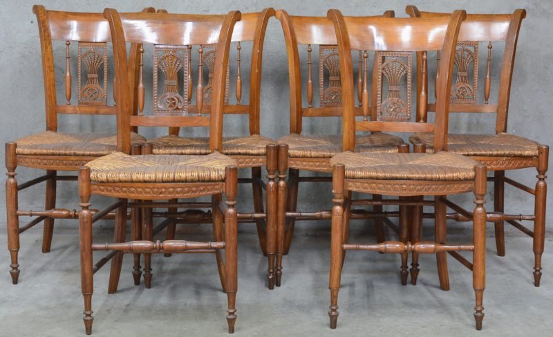 Een reeks van zes notenhouten stoelen met rieten zit en met korenhalmen in de rug.