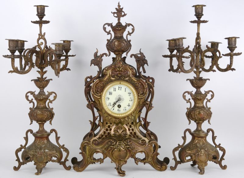 Een driedelig klokstel van koper in Lodewijk XV-stijl, bestaande uit een pendule en twee kandelaars met telkens vijf lichtpunten.