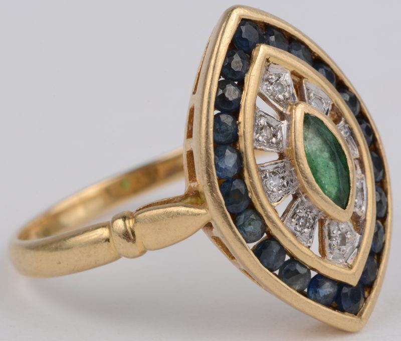 Een 18 karaats wit en geel gouden ring bezet met acht kleine briljantjes en saffieren met een gezamenlijk gewicht van ± 0,40 ct. en een smaragd van ± 0,15 ct.