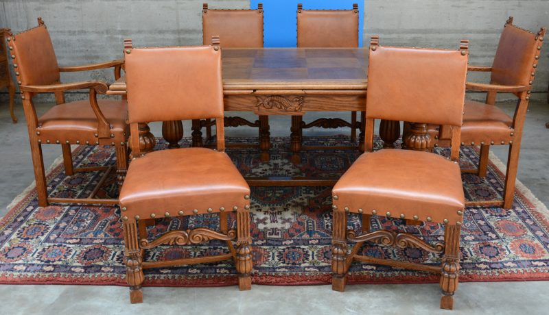 Een verlengbare tafel van gesculpteerd eikenhout met een bijhorende reeks van vier stoelen en twee armstoelen, bekleed met imitatieleder.