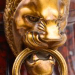 Een schouwpendule van rood marmer met bronzen leeuwenkoppen met ringen aan de zijkant. Werkende staat.