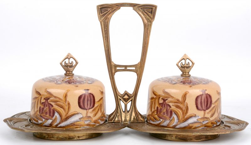 Een serveerschaal in art nouveaustijl van koper met twee aardewerken stolpen, versierd met een bloemenmotief.
