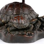 Een bronzen lampvoet in de vorm van schildpadden met een kap in glas en lood, eveneens met schildpadden in het decor.