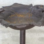 Een gietijzeren vogelbad in de vorm van een blad, versierd met twee vogeltjes.