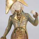 “Officier” & “Dame met parasol”. Een paar beeldjes van verguld brons met ivoren handjes en gezicht en op onyxen voetstukken.
