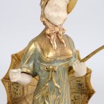 “Officier” & “Dame met parasol”. Een paar beeldjes van verguld brons met ivoren handjes en gezicht en op onyxen voetstukken.
