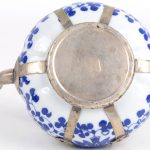 Een pompoenvormig theepotje van Chinees porselein en verzilverd metaal, versierd met een bleuw en wit bloemendecor en met een aapje op het deksel.