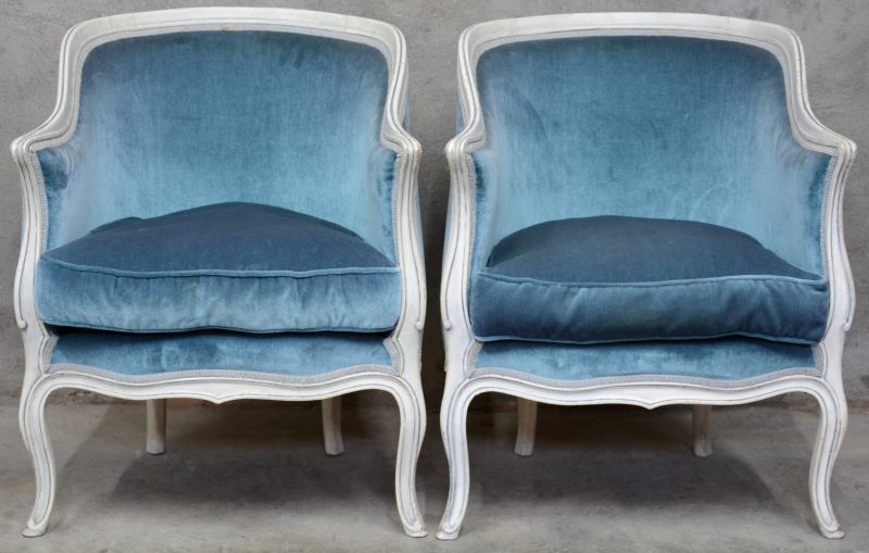 Een paar kuipfauteuils van witgepatineerd hout met blauw fluwelen bekleding.