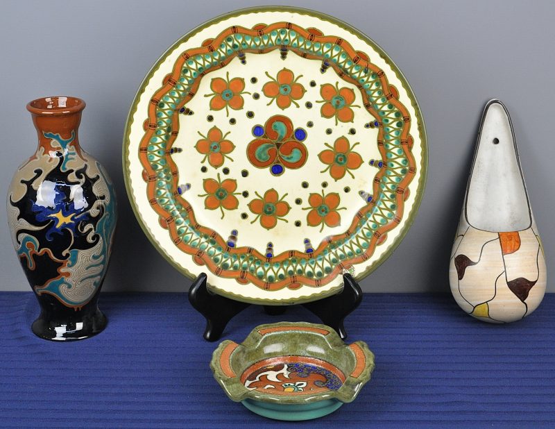 Een lot van vier stuks Gouda-aardewerk, bestaande uit een wandbakje, een asbak, een bord en een vaasje. Het laatste met randschade onderaan.