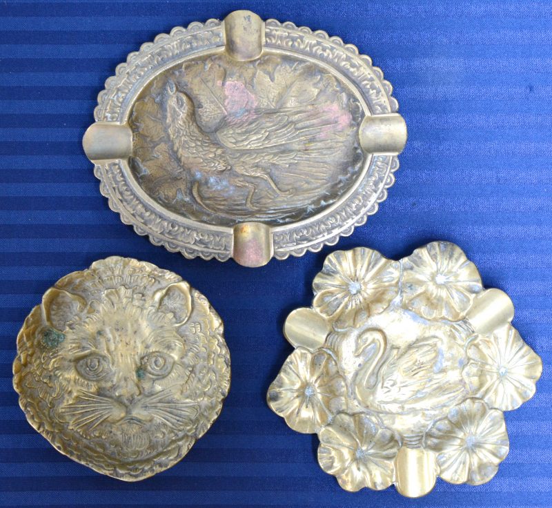 Drie verschillende bronzen asbakken met reliëfdecors, resp. met een zwaan, een vogel en een kattenkop.