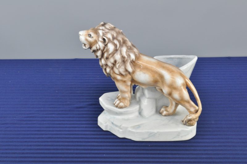 Een sierjardinière van meerkleurig porselein in de vorm van een leeuw op een rots.