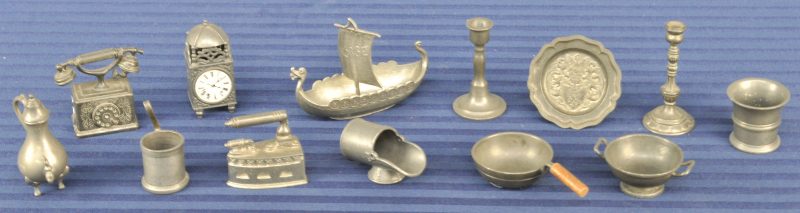 Een lot miniatuur voorwerpjes van tin, bestaande uit een strijkijzer, een telefoon, een vikingschip, een pendule, een sierbord met wapenschild, twee kandelaars, twee pannen, een waterkan, twee emmers en een kolenbak.