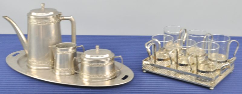 Een driedelig theestel van wit metaal op dienblad. We voegen er zes theeglazen met verzilverd metalen houder en dienblad aan toe.