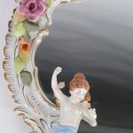 Een spiegel van meerkleurig en verguld porselein, versierd met bloemen en engeltjes in hoogreliëf.