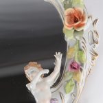 Een spiegel van meerkleurig en verguld porselein, versierd met bloemen en engeltjes in hoogreliëf.