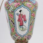 Een lampvoet van meerkleurig Chinees porselein met een decor van personages in cartouches en met een achtergrond van bladeren en vlinders. Op voet van brons in de vorm van gebladerte. Begin XXe eeuw.